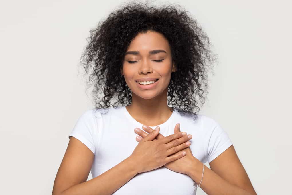 20 Positive Affirmations for Health Anxiety 7 woman with hands on heart, eyes closed and smiling looking grateful and relieved