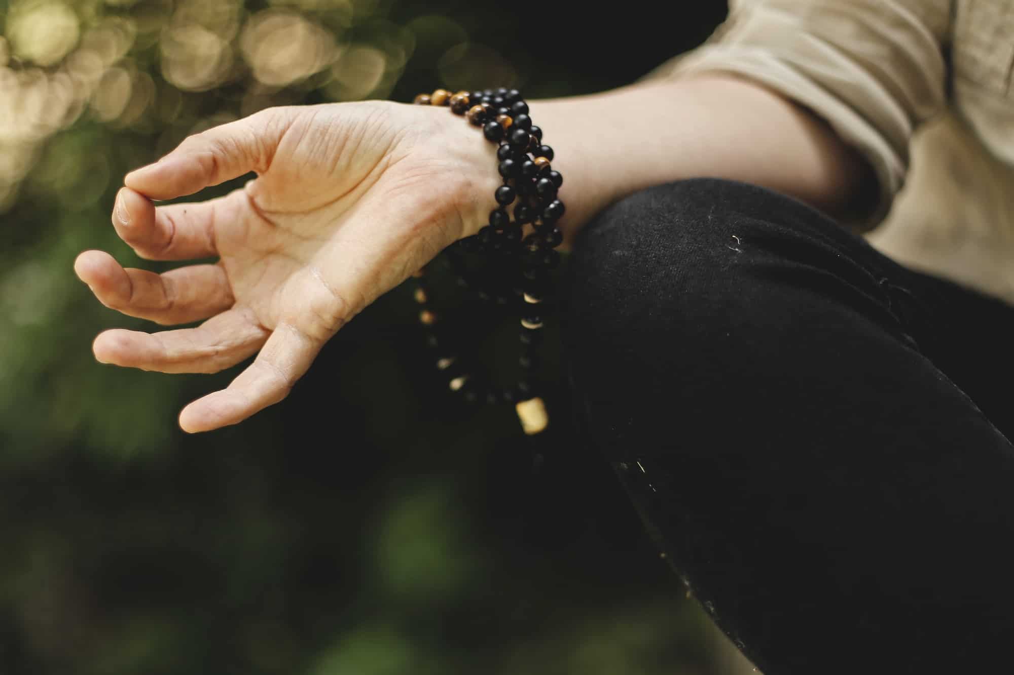 close up of persons hand while meditating with mala beads