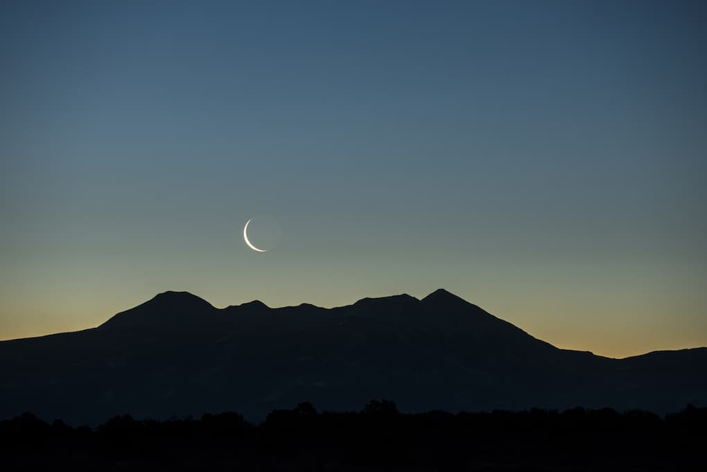 Early morning waning waxing crescent moon rising over graphic silhouetted mountain