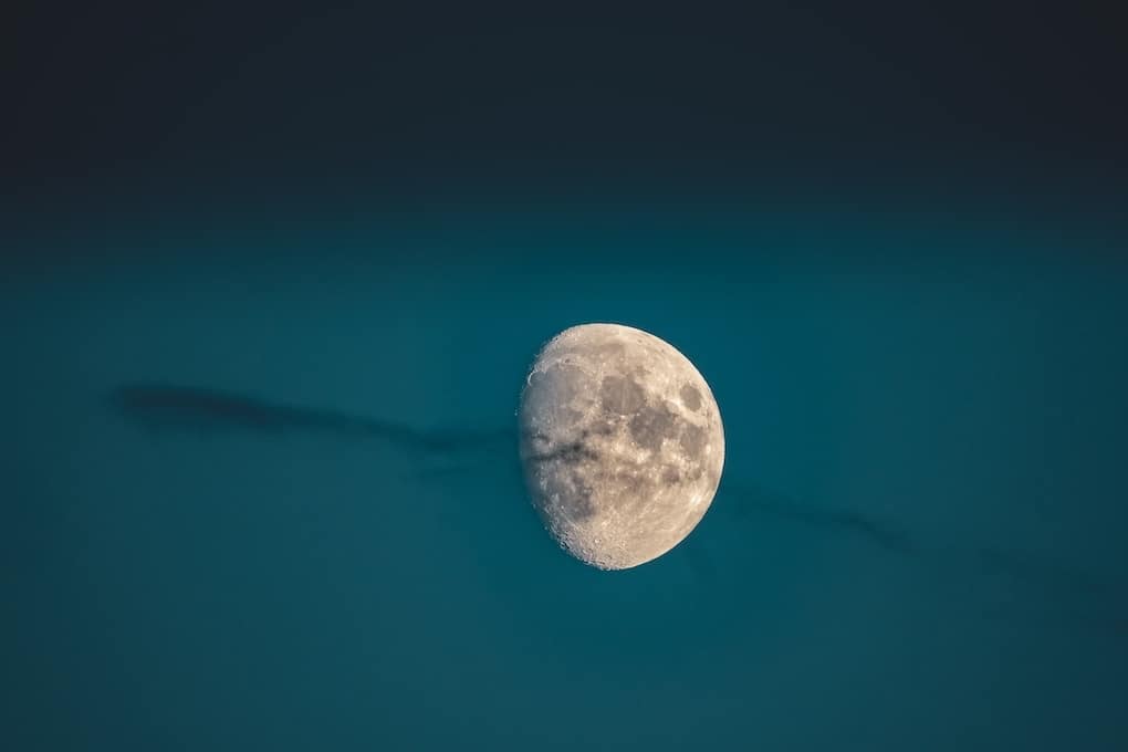 A Guide to Moon Journaling for Sacred Self Care 19 A beautiful shot of a waxing gibbous moon in a dark blue sky with a wispy cloud