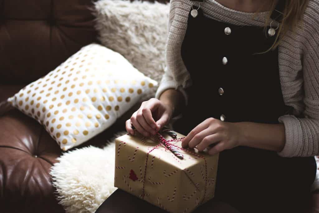 The 21 Best Tarot Gifts for Birthdays and the Holidays in 2024 4 woman in pinafore dress and jumper sat on sofa opening a Christmas gift in candy cane brown wrapping paper