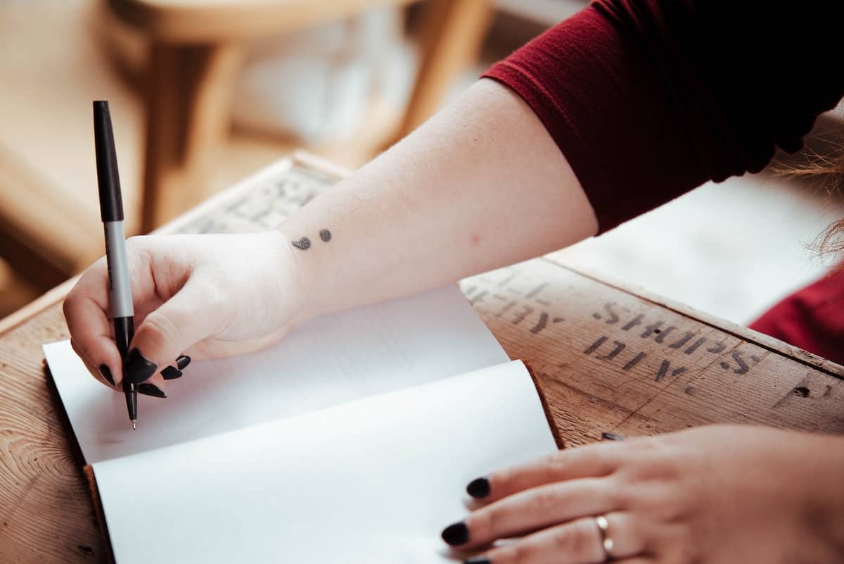 How to JournalSpeak: Journaling for Chronic Symptoms 13 woman writing in journal with semi colon tattoo on wrist