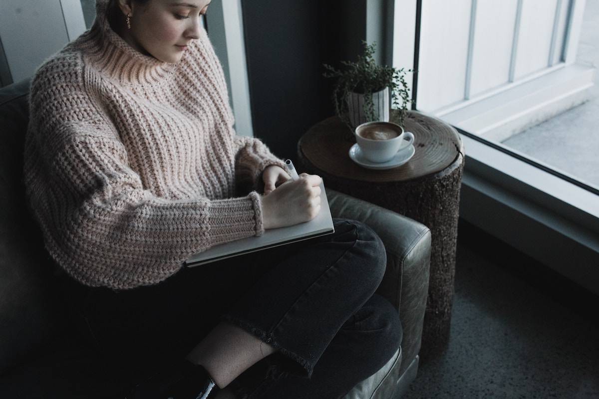 woman sat journaling on the sofa with a coffee by her side