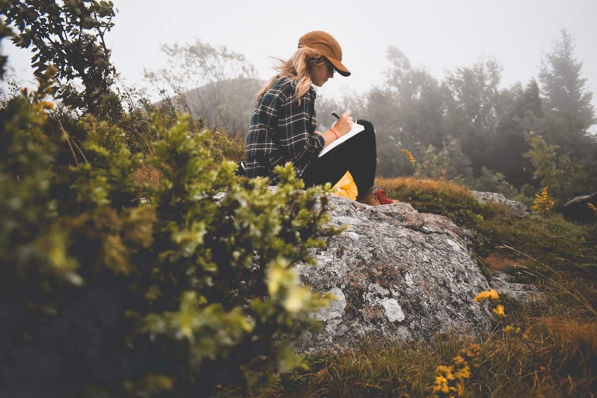 51 Powerful Mindfulness Journal Prompts for Self-Awareness 3 woman sat on rock mindfully journaling in nature