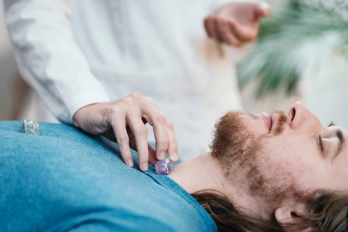 man receiving energy healing treatment. Placing crystal on the throat chakra.