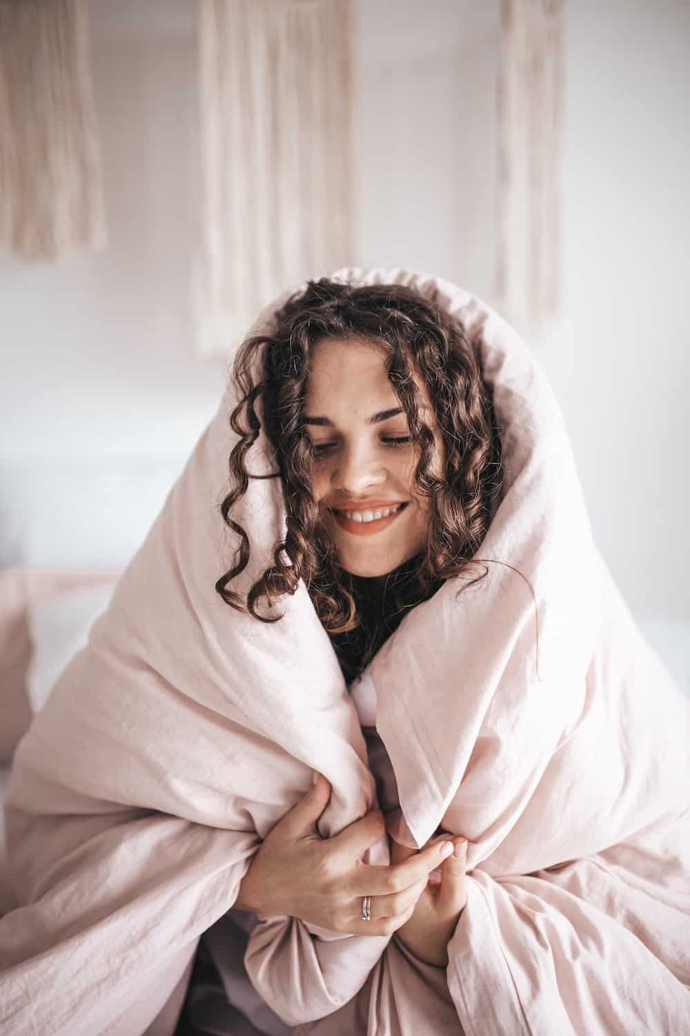 woman giving herself self compassionate hug in duvet while smiling