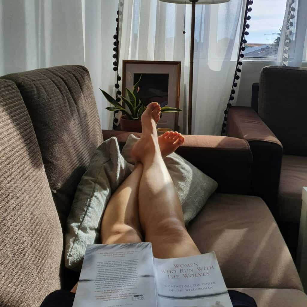 27 Simple Tips to Practice a Slow Living Lifestyle 2 close up of woman's feet up on the couch, living slowly reading "women who run with wolves"