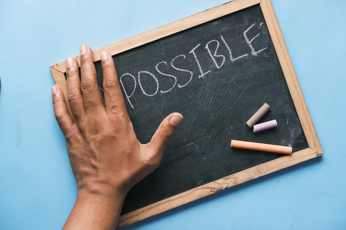 blackboard with the word impossible written on it. a hand is covering the first two letters so that it now reads "possible".