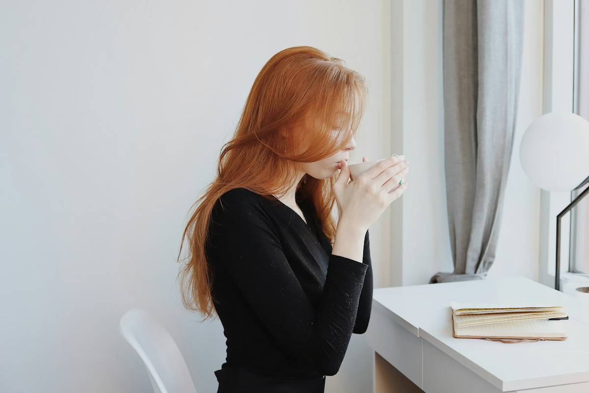 redhead girl drinking a hot drink at desk while journaling