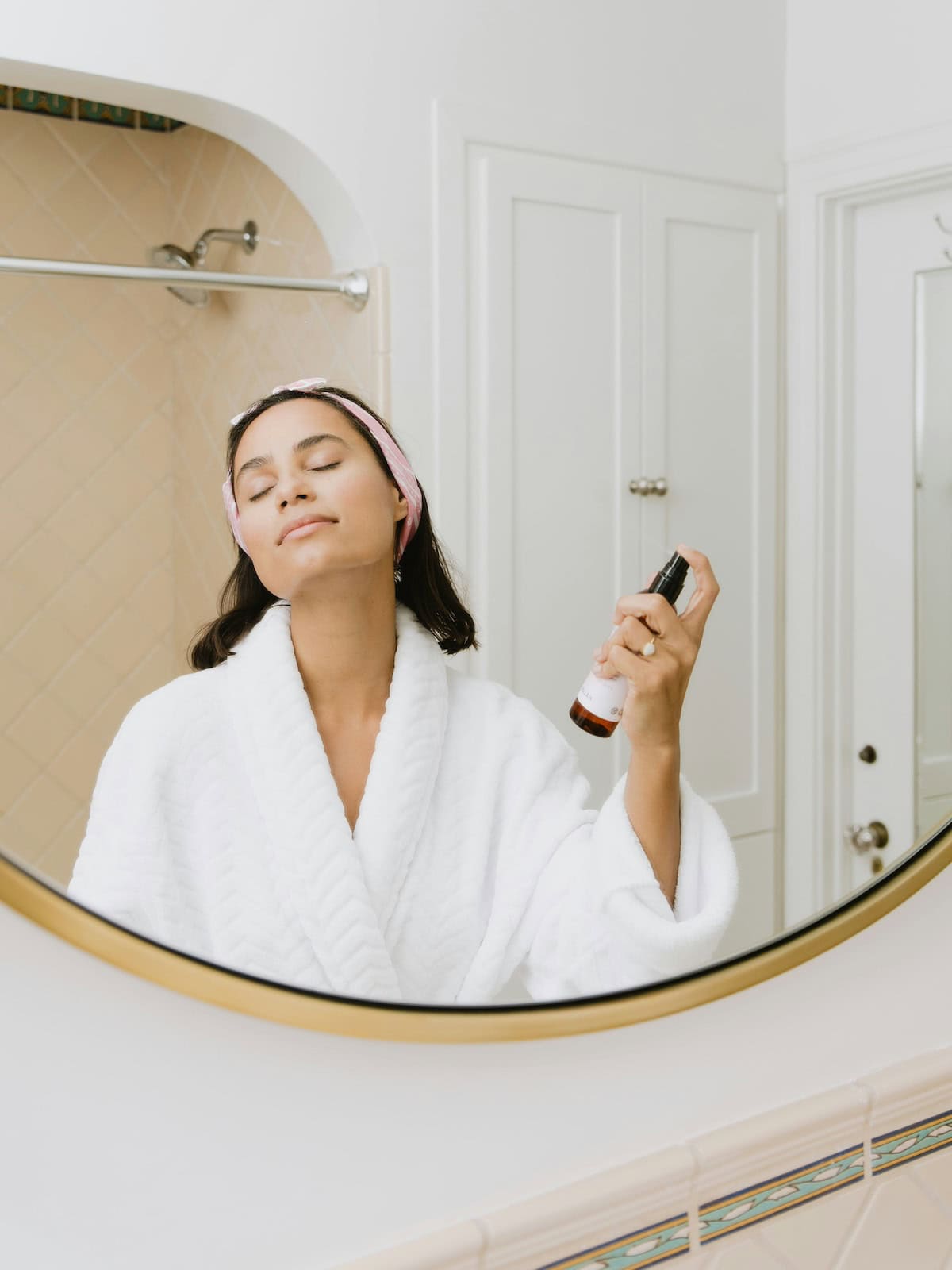 woman pampering herself doing self care in bathrobe, spraying rose water in front of mirror