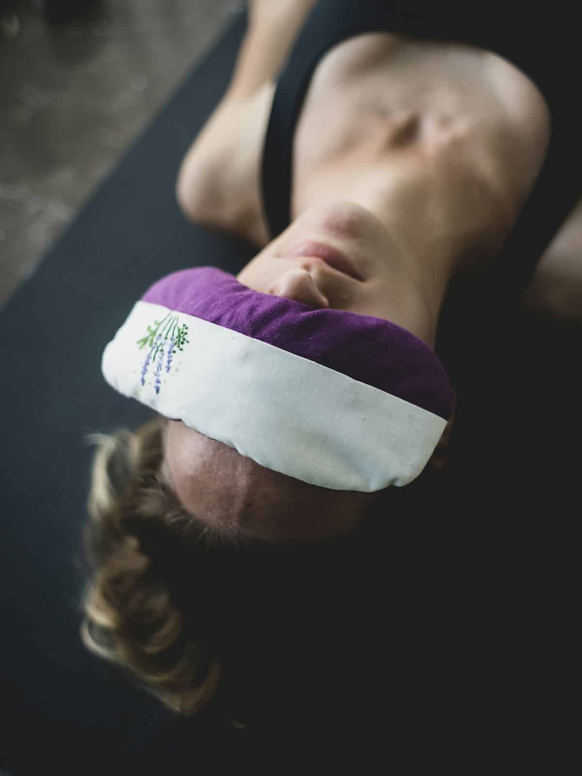 woman laying down doing yoga Nidra with lavender eye pillow on