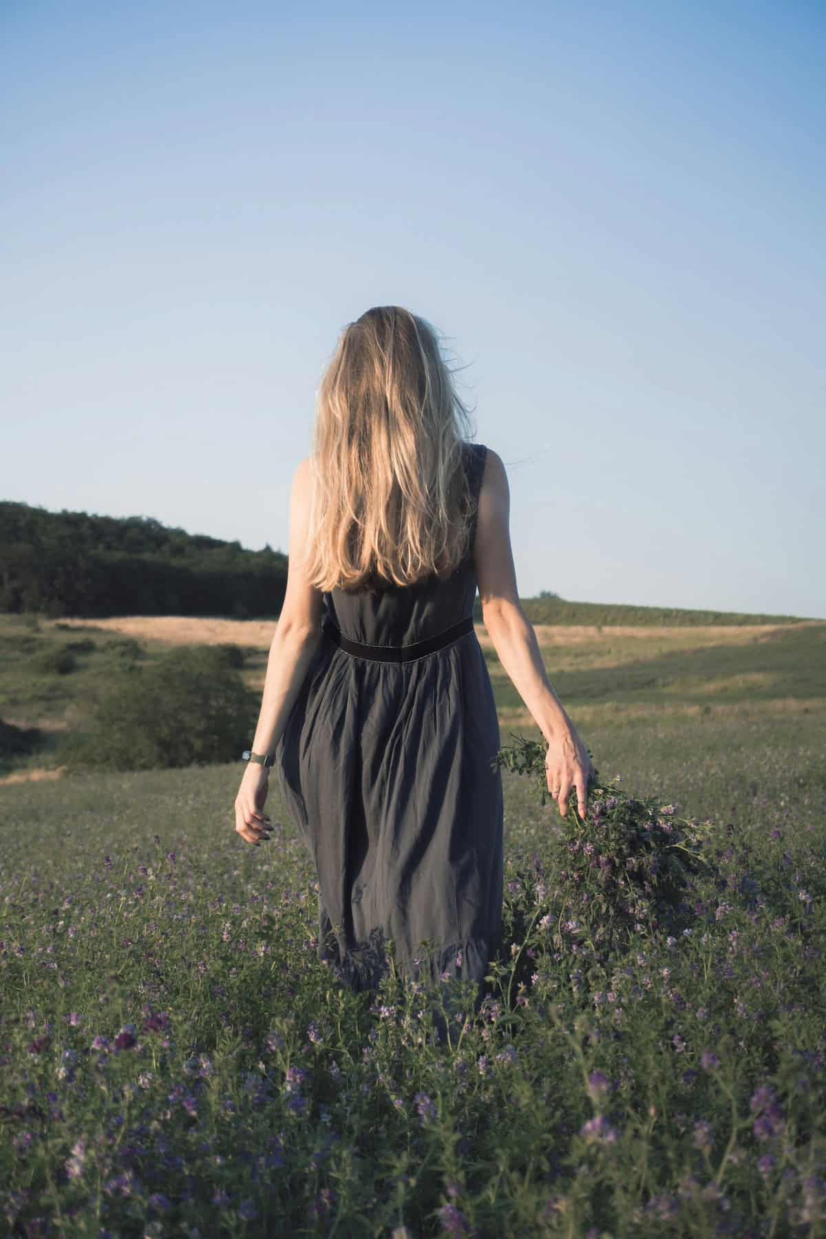 romantic image of girl with long blonde hair walking in fields carrying picked flowers