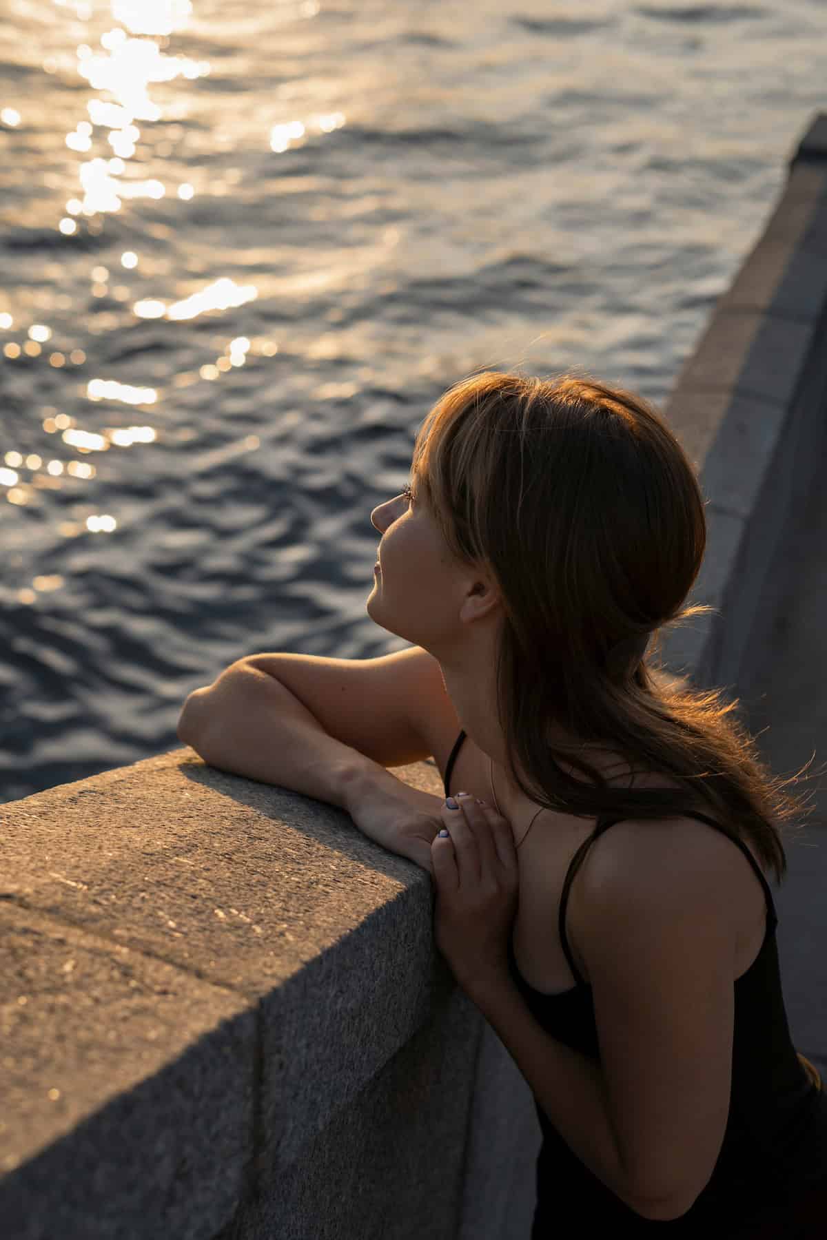 girl romanticising life on solo date, smiling looking out over a wall to the ocean